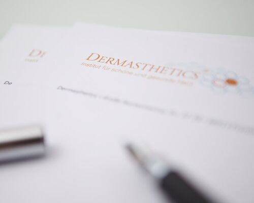 Ein hochwertiger Kugelschreiber auf Briefpapier des Instituts für schöne und gesunde Haut. Das Logo von Dermasthetics ist klar zu sehen. Der Hintergrund ist verwaschen.